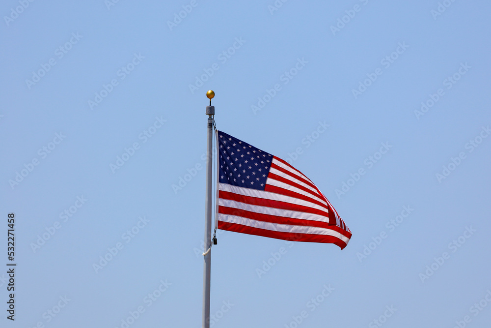 An American flag on a pole flying on the blue sky. An American flag on a pole flying on the blue sky.