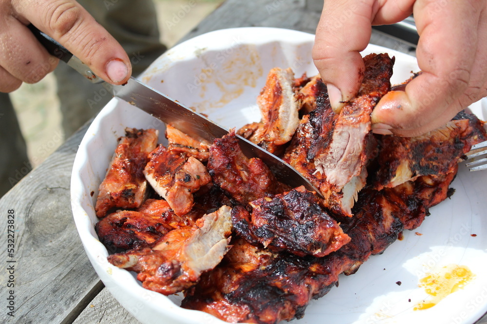 a man cuts pork ribs on the grill with a knife during a picnic