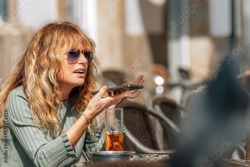 middle-aged woman on terrace sending voice message with mobile phone or smartphone