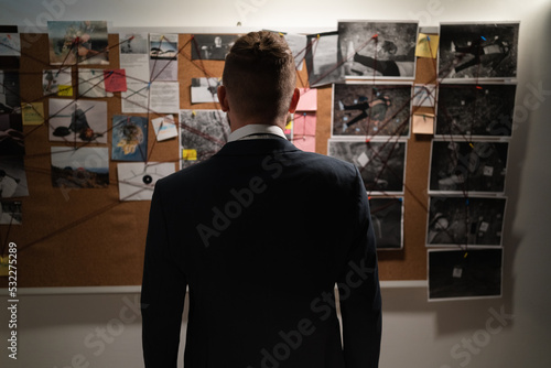 Fotografia Male detective in the office near the blackboard looking for a killer working at night