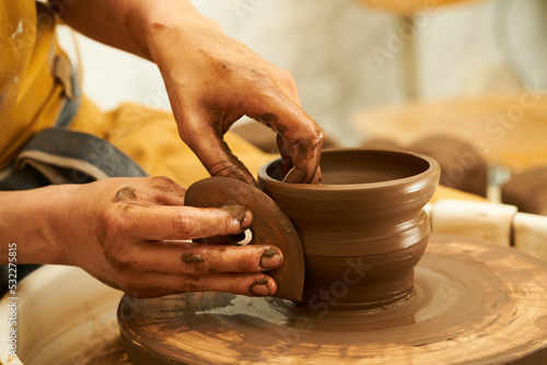 A Potter works with red clay on a Potter's wheel in the workshop..Women's hands create a pot. Girl sculpts in clay pot closeup. Modeling clay close-up. Warm photo atmosphere. 