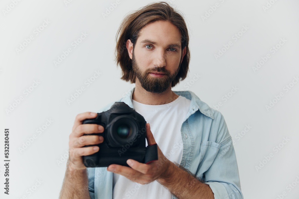Man hipster photographer in a studio against a white background holding a professional camera and setting it up before shooting. Lifestyle work as a freelance photographer Man hipster photographer in a studio against a white background holding a professional camera and setting it up before shooting. Lifestyle work as a freelance photographer