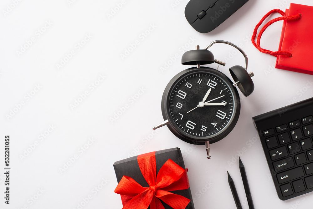 Cyber monday concept. Top view photo of giftbox with ribbon bow alarm clock computer mouse keyboard pencils and red paper bag on isolated white background with copyspace Cyber monday concept. Top view photo of giftbox with ribbon bow alarm clock computer mouse keyboard pencils and red paper bag on isolated white background with copyspace