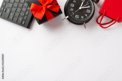 Cyber monday concept. Top view photo of giftbox with red ribbon bow alarm clock keyboard and paper bag on isolated white background with empty space
