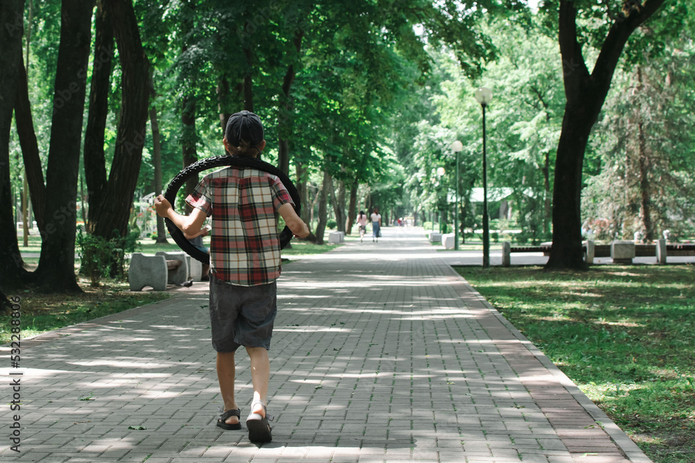 Fototapeta premium A little boy walks in the park, carries a tire from a bicycle