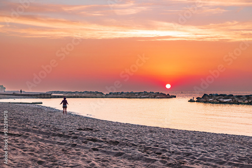 A woman in silhouette walks on a sandy beach as the sun rises over lake ontario in front of her. Shot on Toronto's Kew Beach. photo
