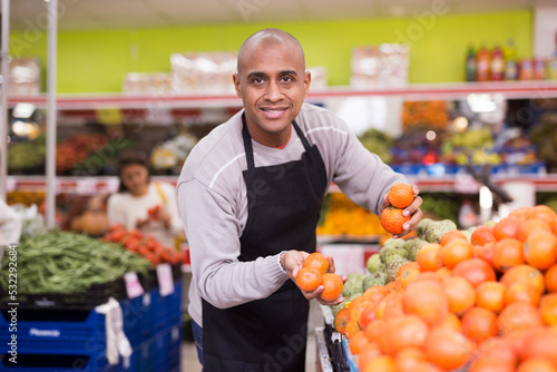 Man in an apron lays out ripe red tomatoes on a supermarket counter
