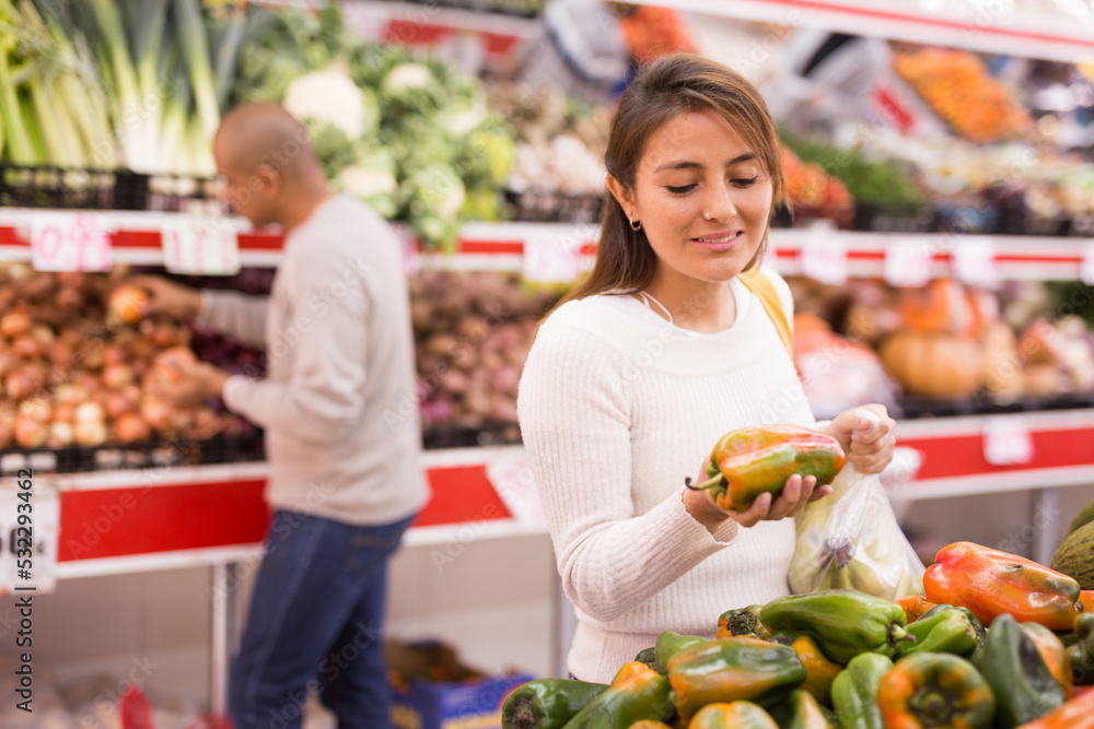 Positive woman picking ripe bell peppers at grocery supermarket