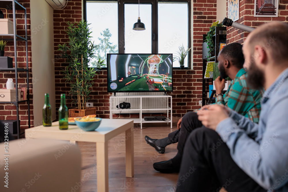 Multiethnic team of men using tv console to play shooting video games, having fun with gaming competition on television. People enjoying teamwork strategy, relaxing with leisure activity.