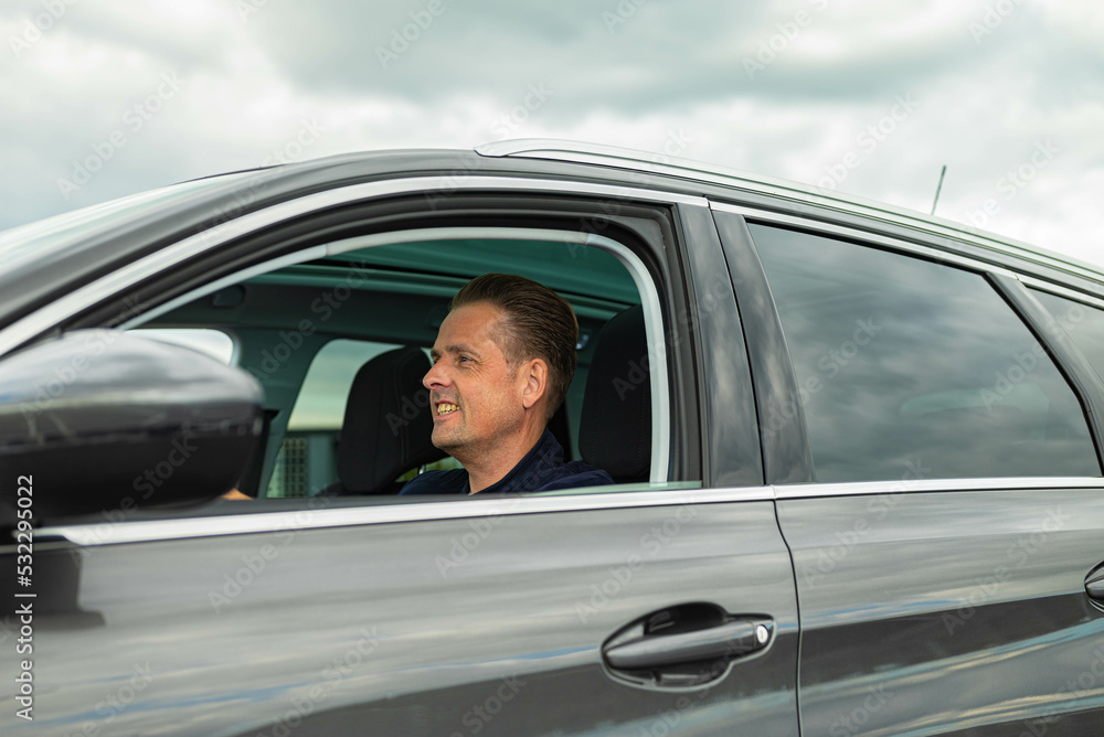 White Caucasian confident man is sitting on the drivers side of a gray black modern car and is looking straight forward at the road ahead. There are no trademarks in the shot. White Caucasian confident man is sitting on the drivers side of a gray black modern car and is looking straight forward at the road ahead. There are no trademarks in the shot.