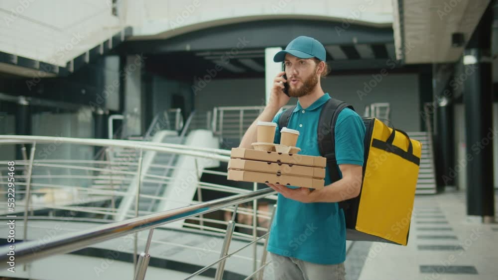 Food Delivery Person Using a Smartphone to Searching for Fast Food Delivery Addresses. Food Delivery Person in Yellow Uniform and With a Thermal Backpack Using Smartphone to Check Order. Fast delivery Food Delivery Person Using a Smartphone to Searching for Fast Food Delivery Addresses. Food Delivery Person in Yellow Uniform and With a Thermal Backpack Using Smartphone to Check Order. Fast delivery