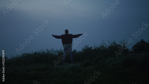Lonely guy walking in misty field. Back view man raising hands in air