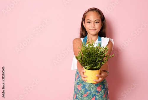 little child girl holding a plant over pink background.
