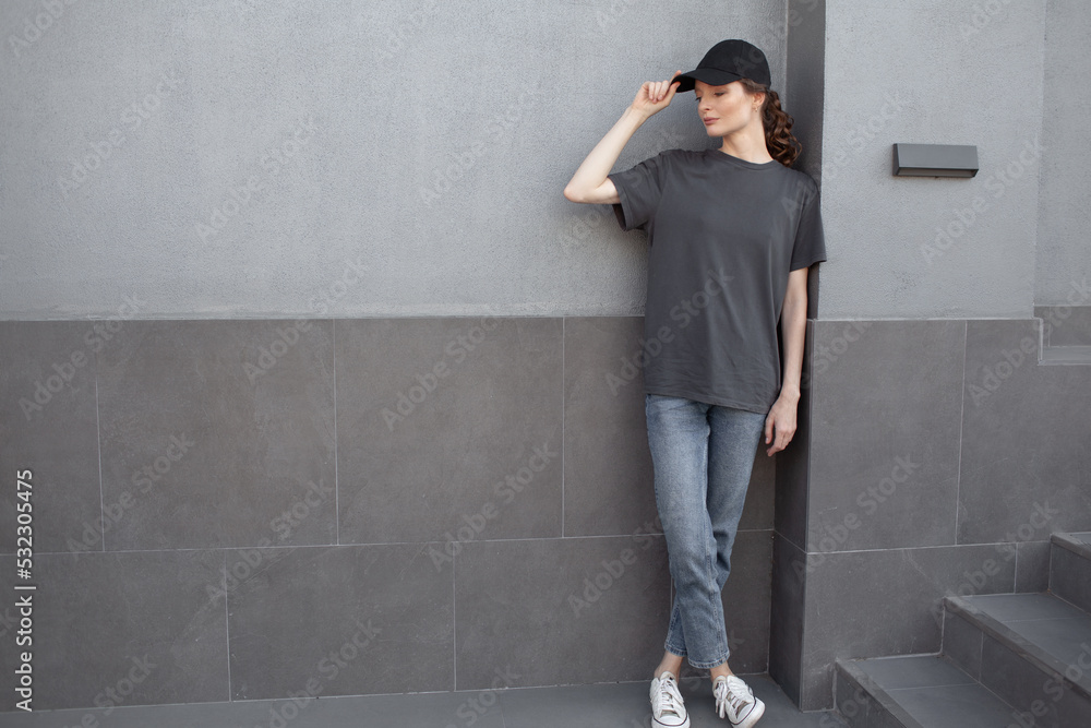 A beautiful girl is wearing a grey t-shirt, cloth cap and jeans posing against the background of a wall. fashion outfit for the city, minimalism urban style clothing A beautiful girl is wearing a grey t-shirt, cloth cap and jeans posing against the background of a wall. fashion outfit for the city, minimalism urban style clothing