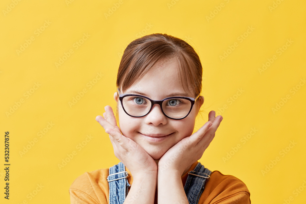 Closeup portrait of cute girl with Down syndrome looking at camera against yellow background in studio Closeup portrait of cute girl with Down syndrome looking at camera against yellow background in studio