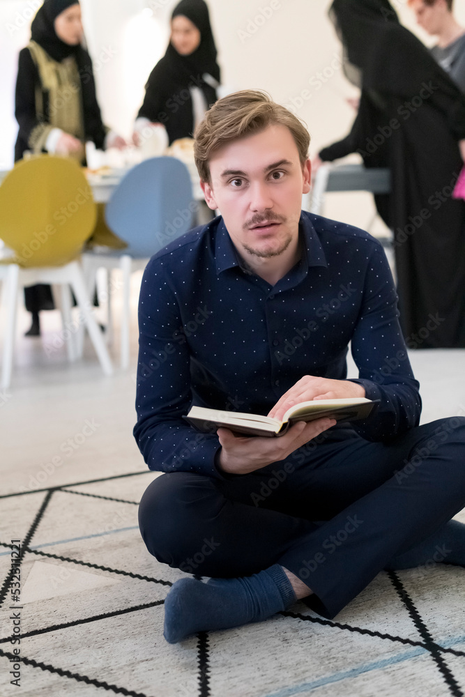 Young muslim man sitting on the floor while reading holy book Quran before iftar dinner during a ramadan feast at home Young muslim man sitting on the floor while reading holy book Quran before iftar dinner during a ramadan feast at home