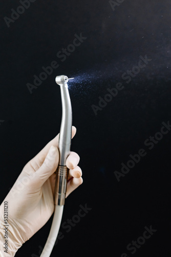 Dentist hand with drill illustrates the operation of the dentist dental drill machine with water. Dentist's hands with blue gloves working with dental drill in dental office. Close up, selective focus