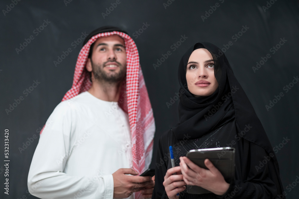Young muslim business couple in fashionable hijab dress using smartphone and tablet in front of black background