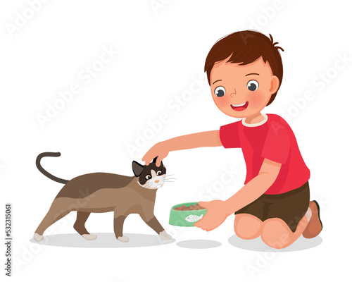 Cute little boy feeding his pet cat with animal food at home