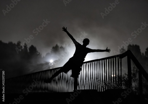 on a foggy evening, a dark human silhouette against the background of the old bridge, illuminated by the lanterns of the forest part