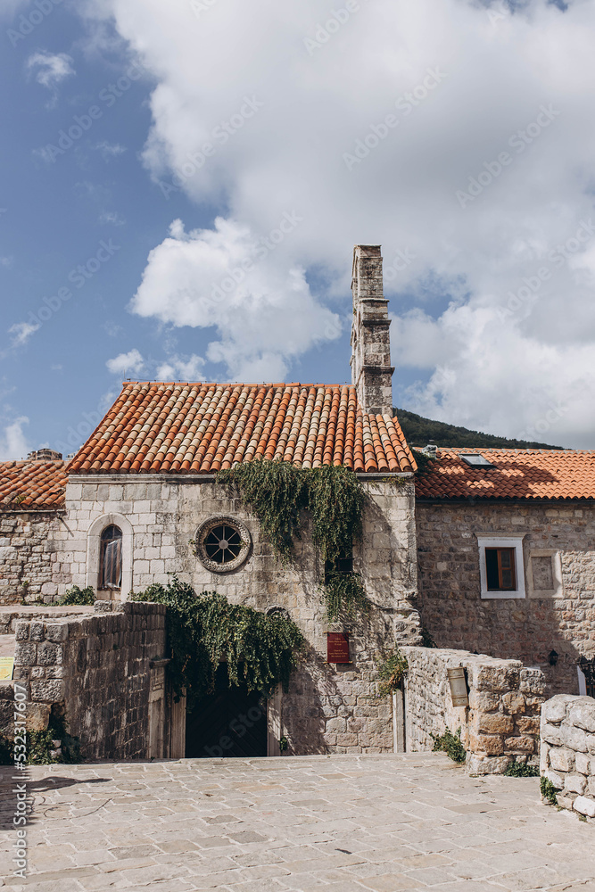 Budva, Montenegro - September 18, 2021: red rooftops in old castle listed as UNESCO World Heritage Sites. Old church on a rock. Tourism and traveling concept. Attraction for european, world tourists Budva, Montenegro - September 18, 2021: red rooftops in old castle listed as UNESCO World Heritage Sites. Old church on a rock. Tourism and traveling concept. Attraction for european, world tourists