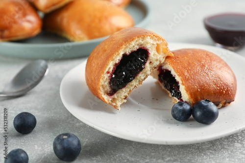 Delicious baked patties with jam and blueberries on light grey table, closeup