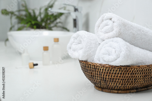 Rolled bath towels in wicker bowl indoors, space for text