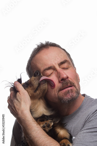 A man and his loving dog licking his face on a white background.