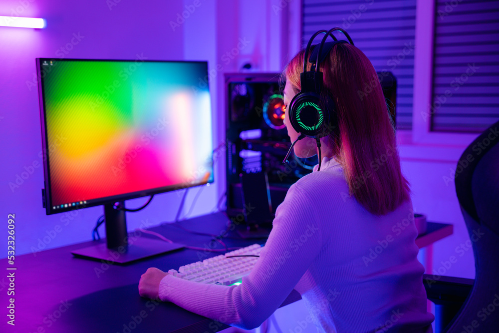 Asian professional gamer playing online video game on desktop computer PC have colorful neon LED lights, young woman in gaming headphones using computer for playing game at home Asian professional gamer playing online video game on desktop computer PC have colorful neon LED lights, young woman in gaming headphones using computer for playing game at home