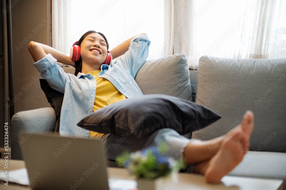 Happy asian woman listening to music while leaing back on couch.