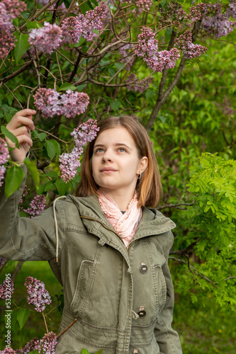 Portrait of a young teenage girl in the garden, a bush of blooming lilacs in the spring. High quality photo