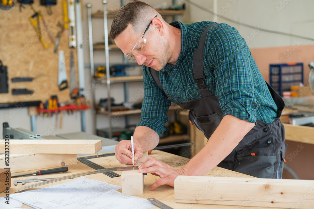 A carpenter measures wooden planks and makes marks with a pencil in a workshop.