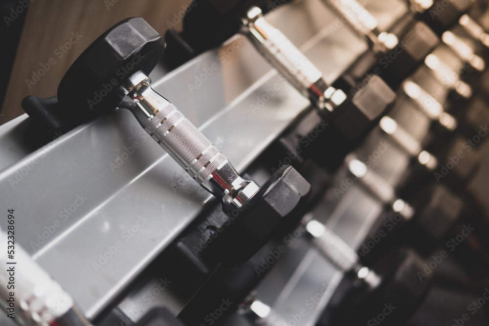 Rows of metal dumbbells on rack for strength training in gym. Close up