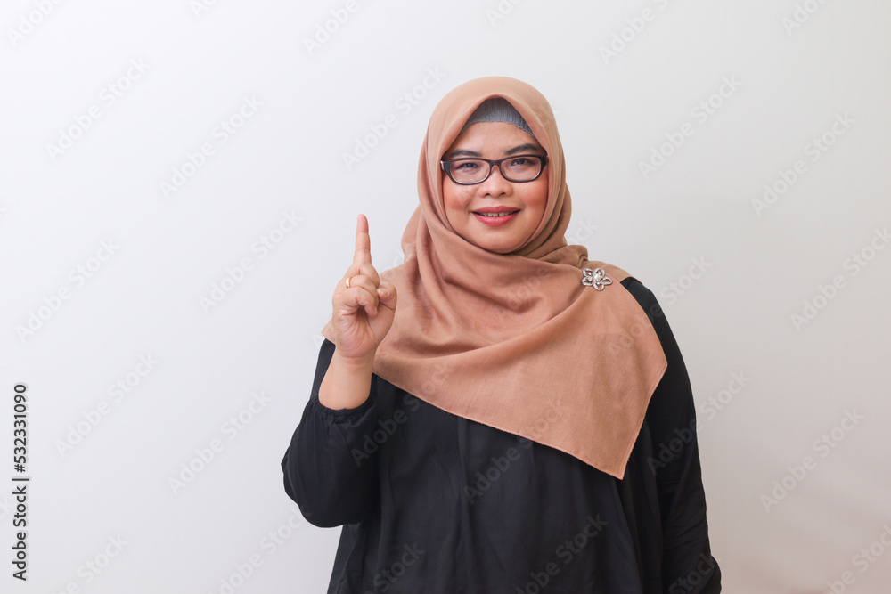 Portrait of cheerful Asian woman with hijab, pointing up her forefinger and reminding something to do. Advertising concept. Isolated image on white background Portrait of cheerful Asian woman with hijab, pointing up her forefinger and reminding something to do. Advertising concept. Isolated image on white background