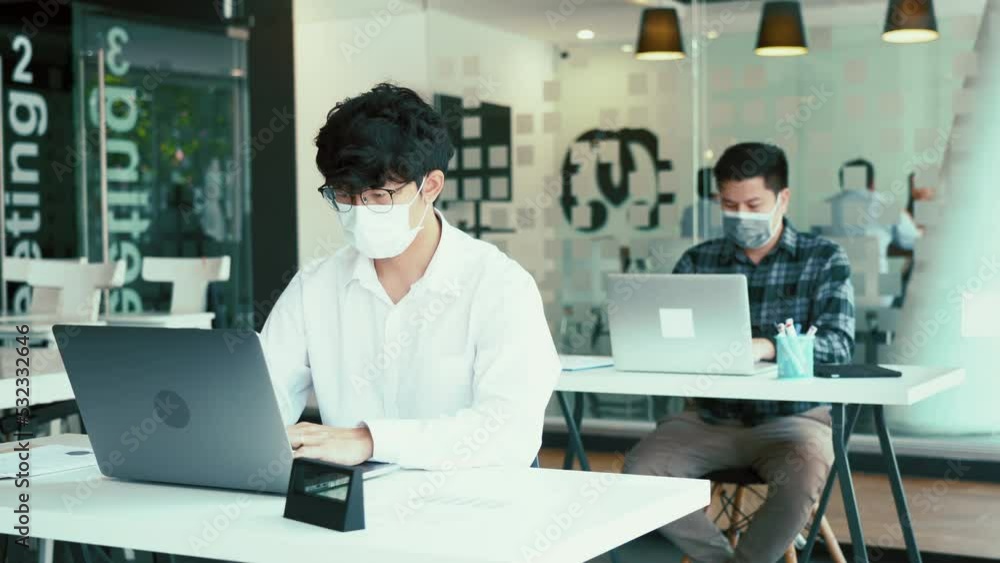 Asian colleague works while wearing a mask in the office during COVID-19. Asian colleague works while wearing a mask in the office during COVID-19.