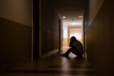 Depressed man sitting on the floor with his head down, silhouette of stressed young man holding his head in the hallway