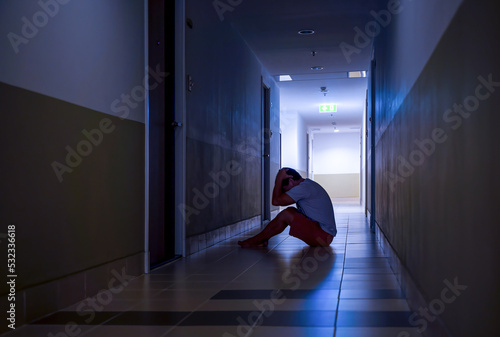 Depressed man sitting on the floor with his head down  silhouette of stressed young man holding his head in the hallway