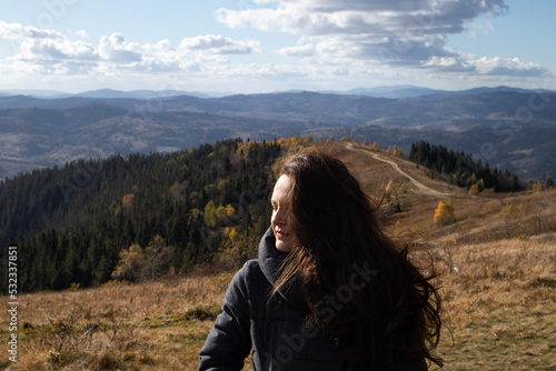 Young happy brunette woman is standing in front of mountains landscape