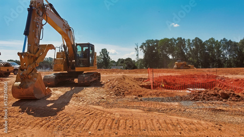 digger and bulldozer grading dirt field with construction fence 