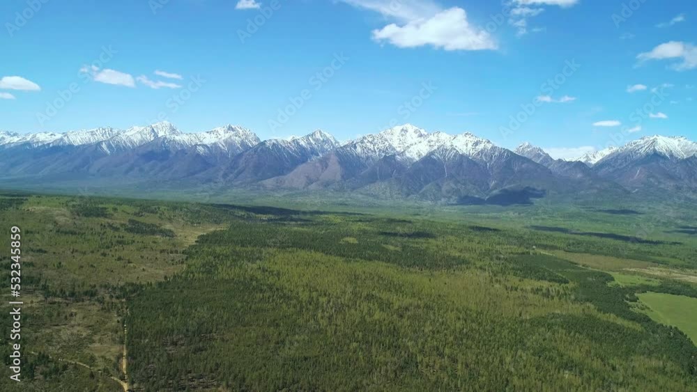 Aerial panoramic landscape of snow capped Sayan Mountains, valley and green forest on a bright sunny day. Picturesque scenery of Siberian nature Aerial panoramic landscape of snow capped Sayan Mountains, valley and green forest on a bright sunny day. Picturesque scenery of Siberian nature