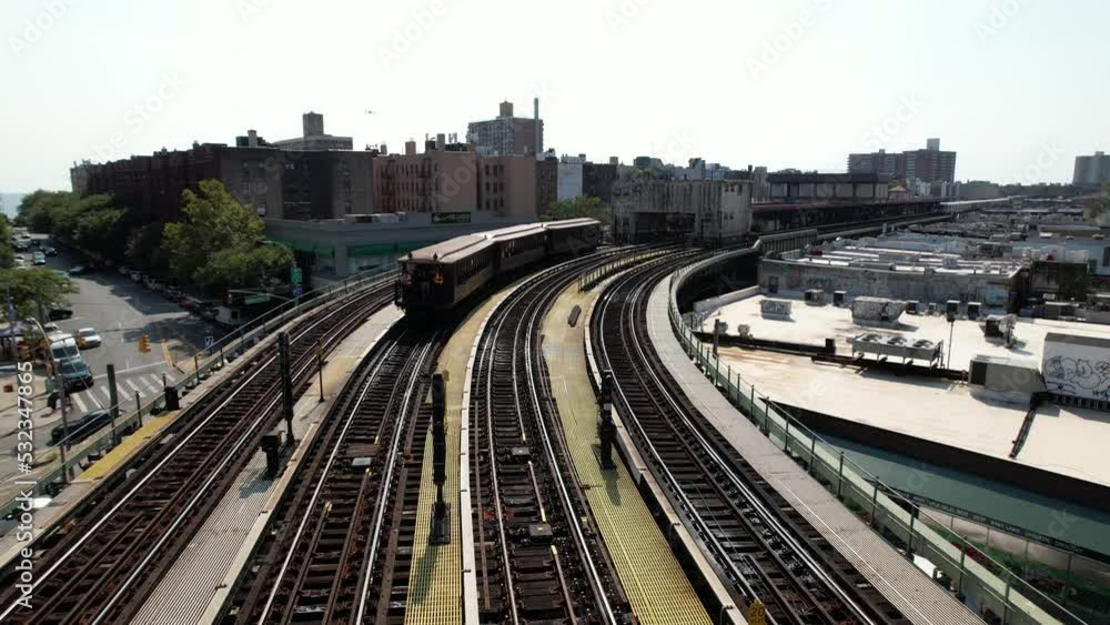 An aerial view of train tracks with a vintage BU Gate Car built in 1904 travelling away from the camera on a sunny day. The drone camera is stationary over the center of the elevated tracks. An aerial view of train tracks with a vintage BU Gate Car built in 1904 travelling away from the camera on a sunny day. The drone camera is stationary over the center of the elevated tracks.