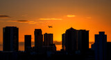 Airliner Departing a City at Sunset with Buildings Silhouetted.