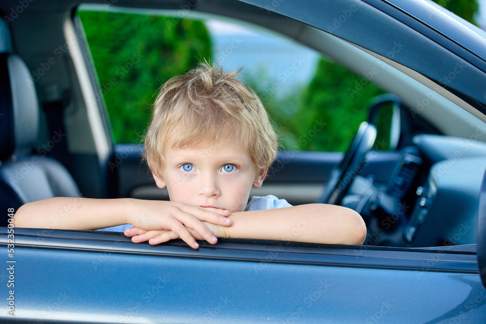 Cute calm boy is sitting in the passenger seat of a car, with his hands folded in the open window. Small child in the passenger seat of a car looks out of an open window Cute calm boy is sitting in the passenger seat of a car, with his hands folded in the open window. Small child in the passenger seat of a car looks out of an open window