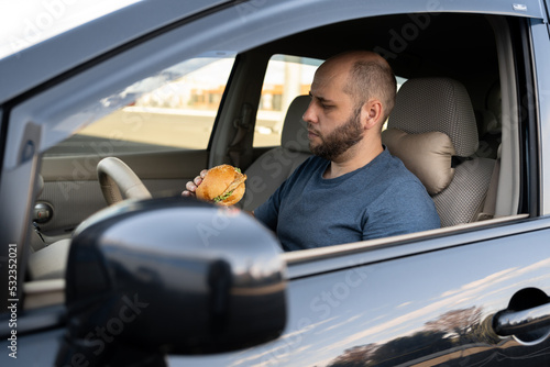driver man at the wheel while eating food in the traffic, eat hamburger in car. urban life.