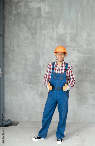 Young arabic man over grey concrete wall wearing contractor uniform and safety helmet happy with big smile doing ok sign, thumb up with fingers excellent sign