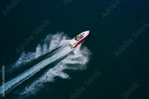 Luxurious Red White motorboat rushes through the waves of the blue Sea. Boat fast moving aerial view. Luxurious boat fast movement on dark water.