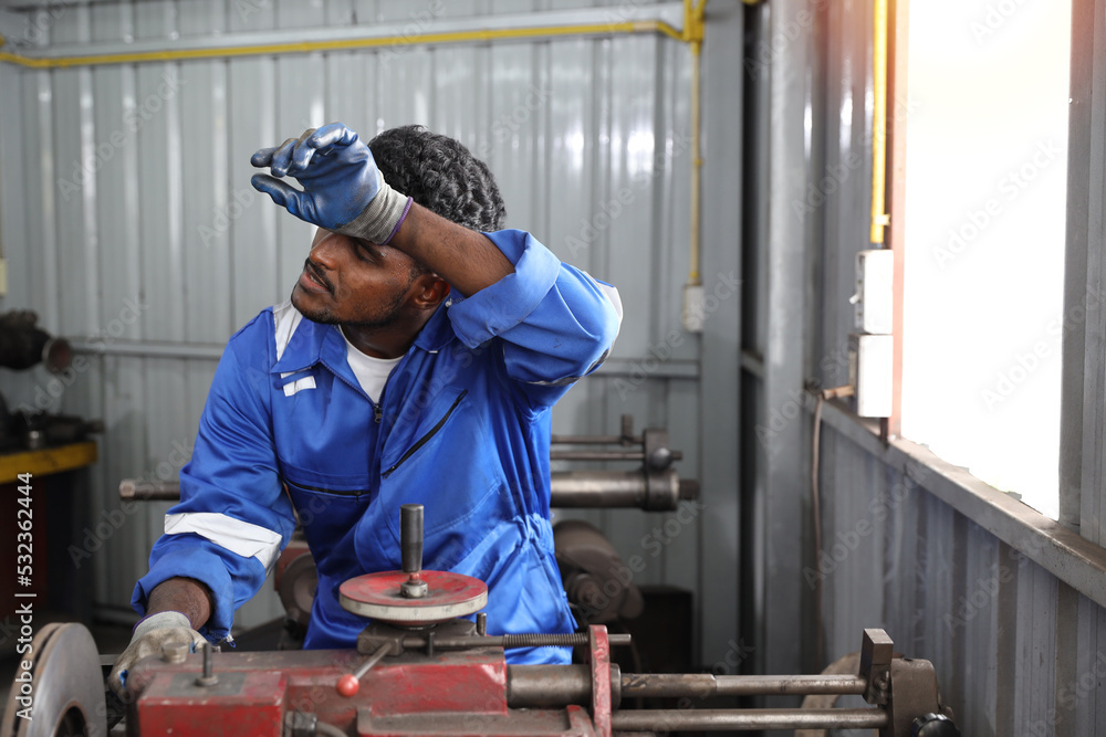 Tired heat and hot technicain mechanic man in uniform using metal lathe