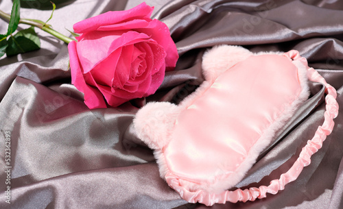  sleeping mask on a silk bedding sheet and pink rose, romantic evening concept, dating and love, relationship.