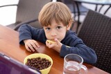 Unhappy little boy sit at table and watch cartoon on tablet computer top view. Kid of kindergarten age eat chocolate balls with milk and drink water. Autism, mental disease, deviation, health problem