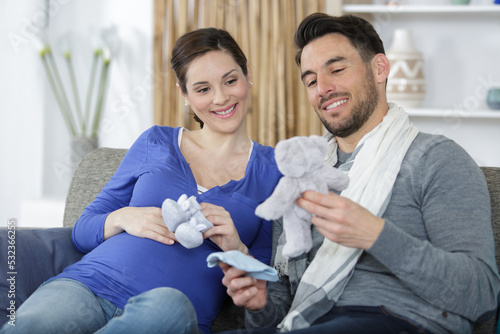 pregnant couple holding baby shoes and teddy